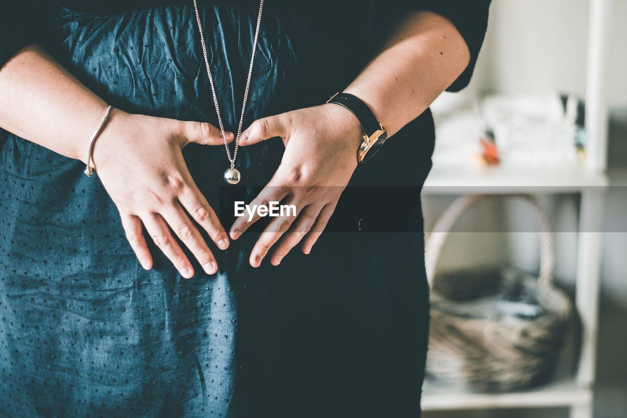 Midsection of pregnant woman making heart shape on abdomen