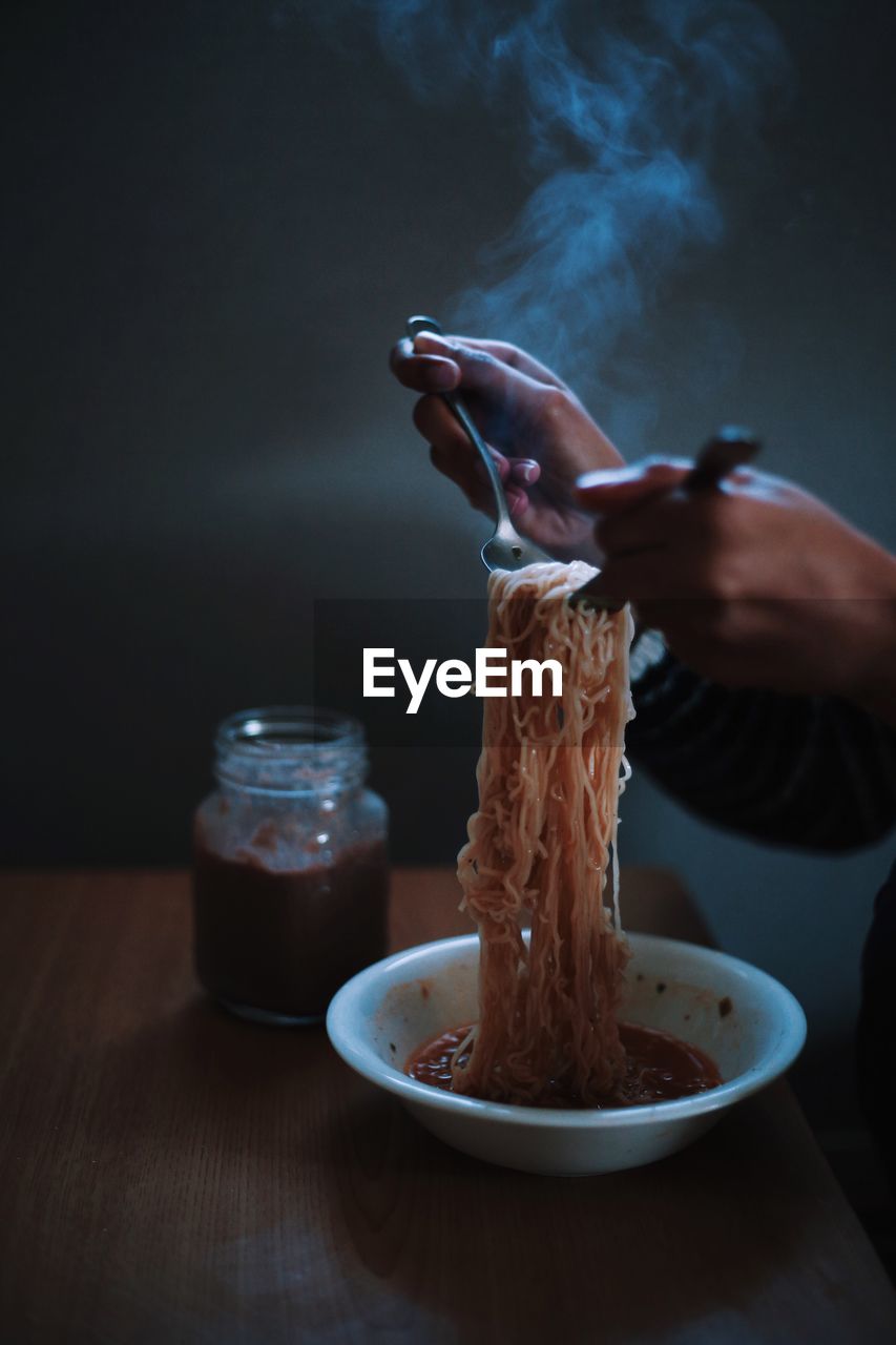 Cropped hands holding noodles at table