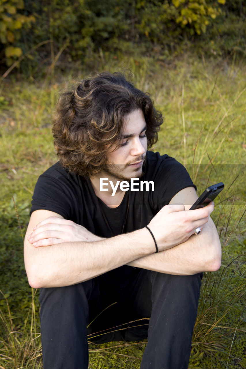 Young man using smart phone while sitting on grassy field