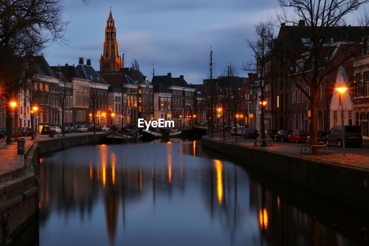 Illuminated buildings by canal against sky at night