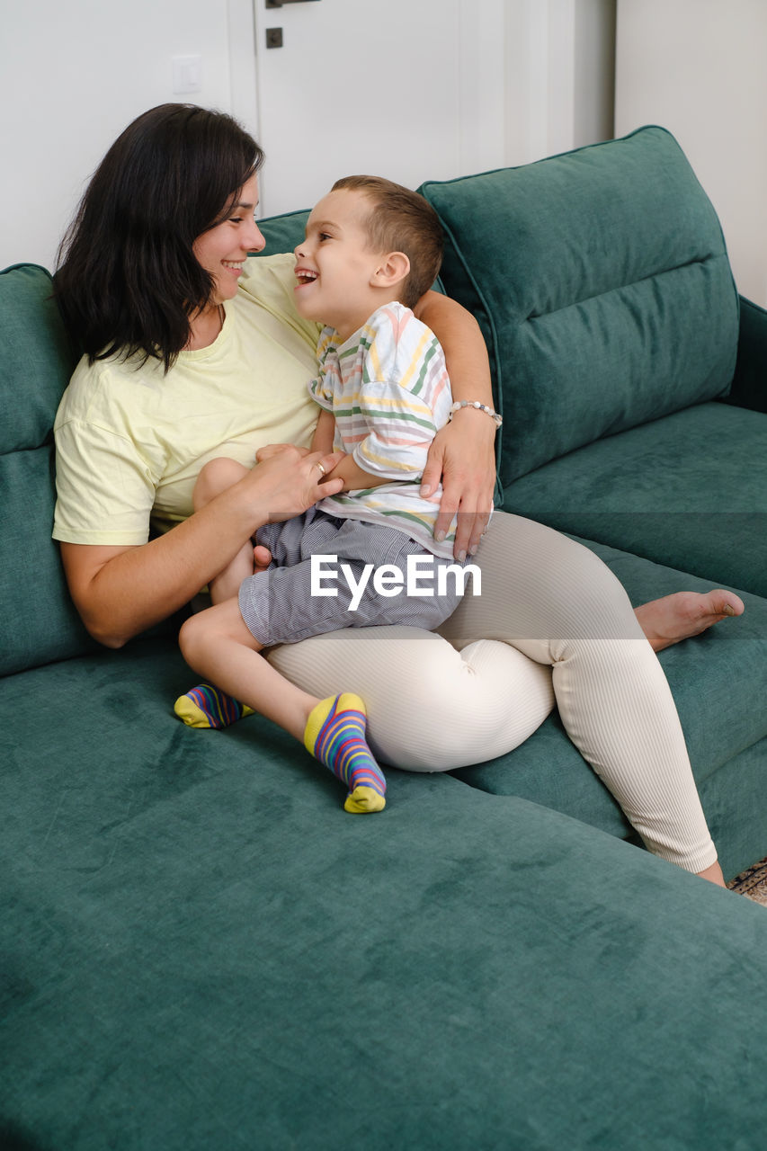 Mother holding child living with disability on sofa woman hugging boy with cerebral palsy at home