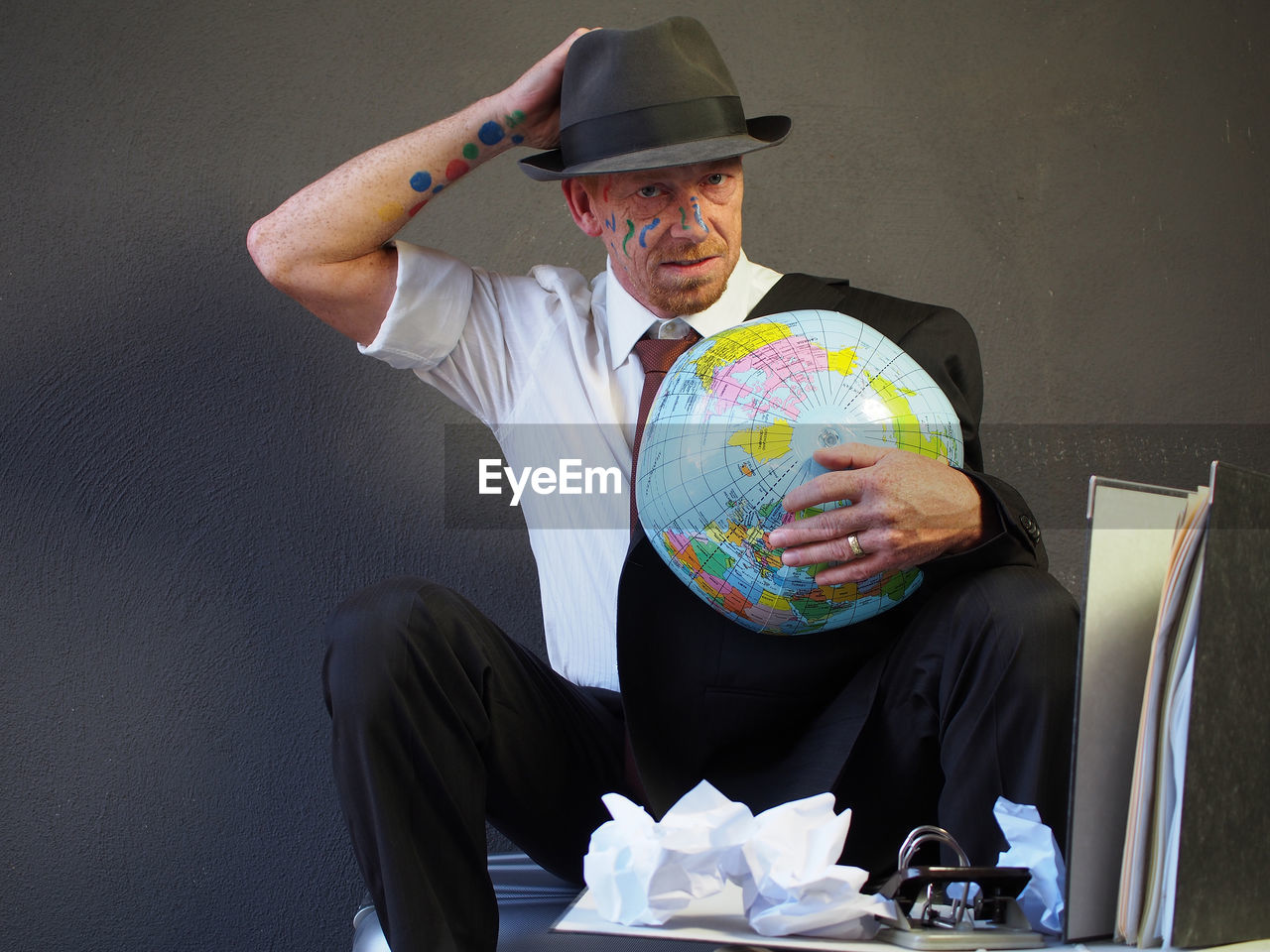 Portrait of businessman with face paint holding globe while standing at office