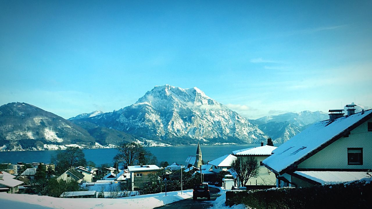 Houses by river and snow covered mountains against sky