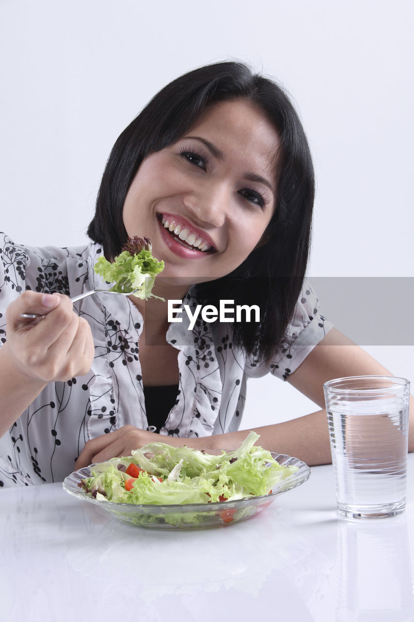 Woman eating vegetable salad at table against white background