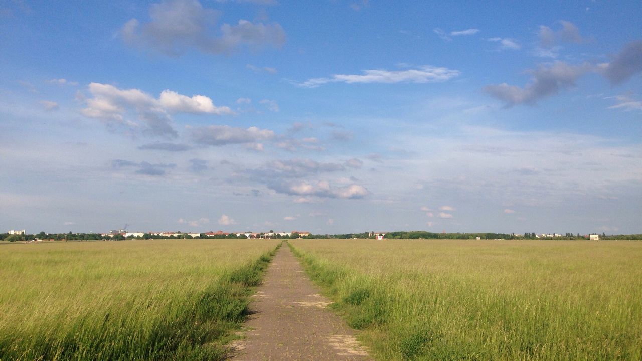 Road on grassy field against sky