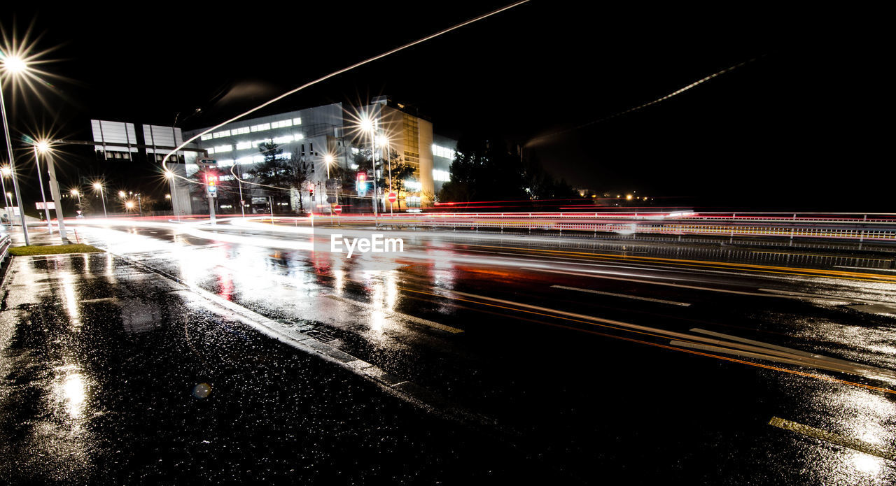 Light trails on wet street against sky at night