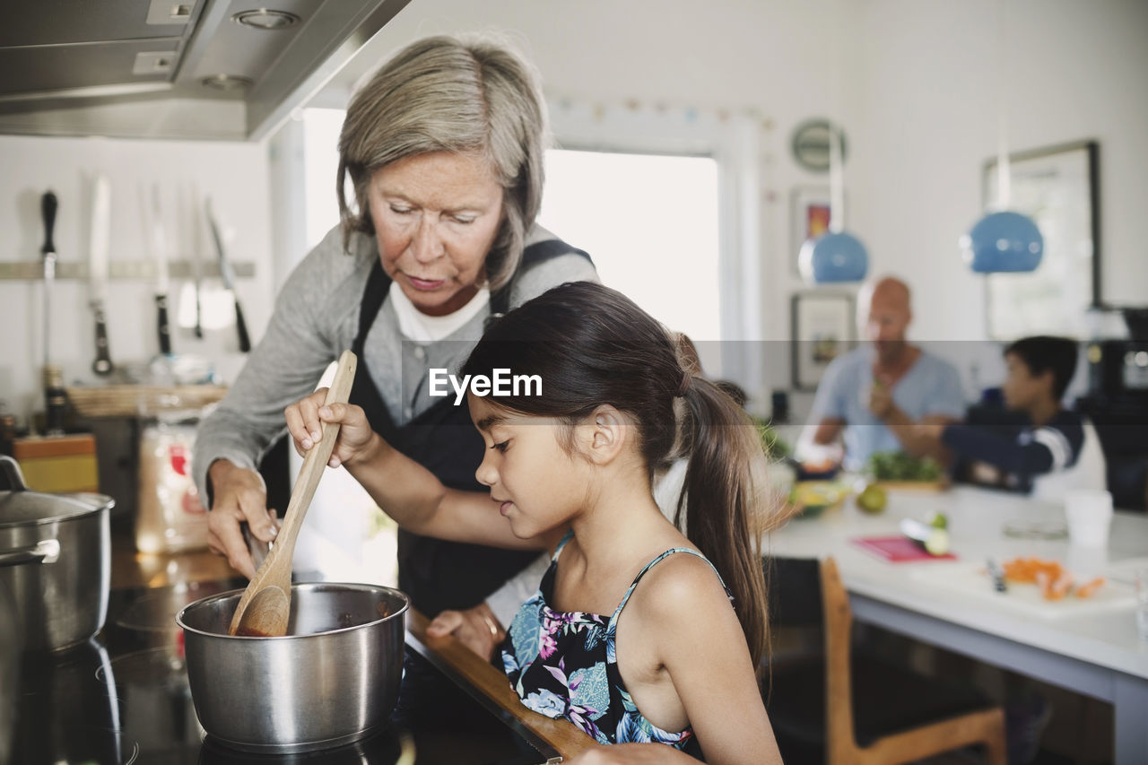 Grandmother looking at girl cooking at kitchen counter