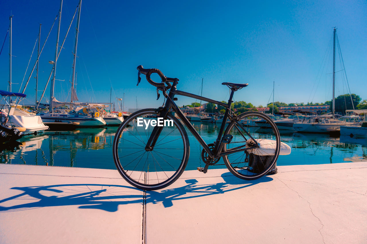 Road bike in front of sailboats moored in harbor against clear blue sky