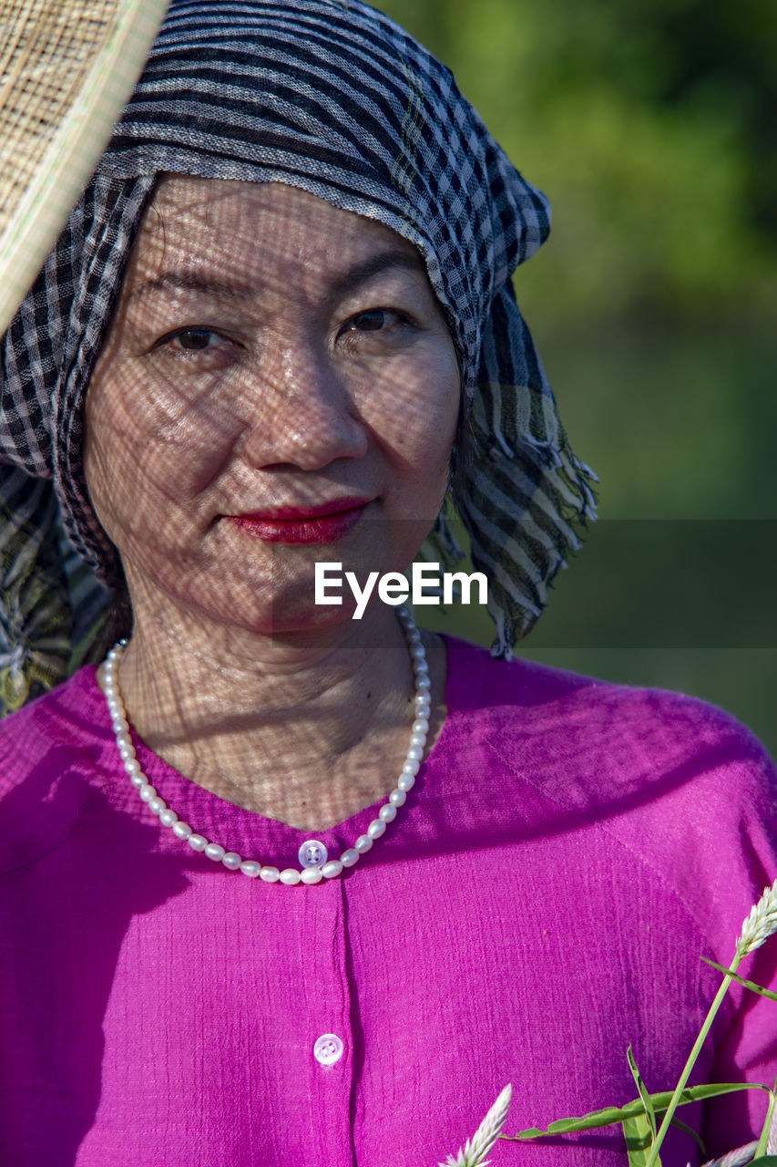 portrait, adult, one person, women, clothing, headshot, person, human face, female, looking at camera, senior adult, front view, jewelry, emotion, smiling, purple, lifestyles, necklace, close-up, mature adult, traditional clothing, pink, focus on foreground, wrinkled, fashion accessory, hat, nature, human head, outdoors, happiness