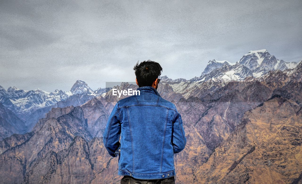 Rear view of man standing on mountain against sky