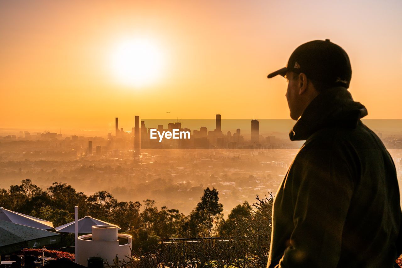 Man standing against cityscape and sky during sunset