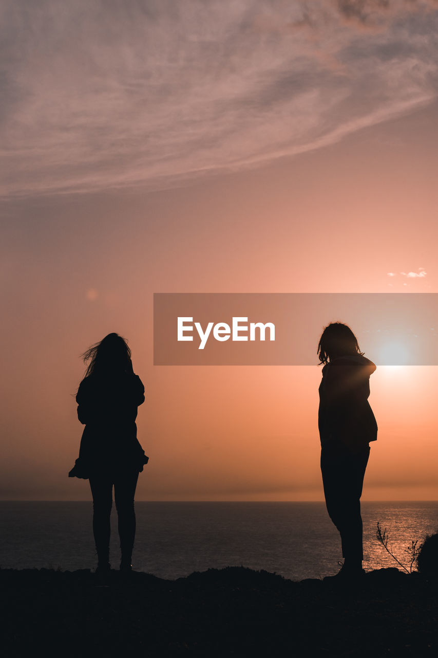 Silhouette friends standing on beach against sky during sunset