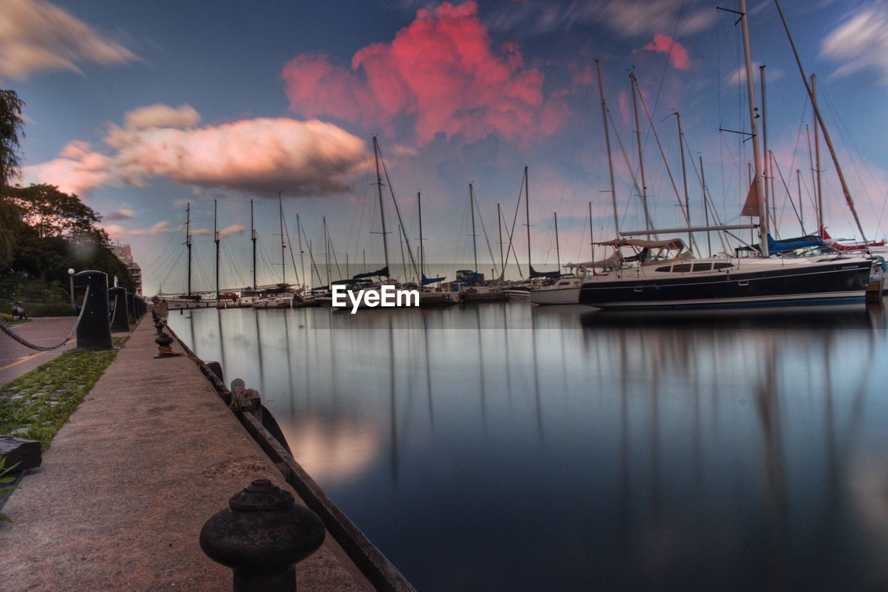 Sailboats moored on harbor against sky during sunset