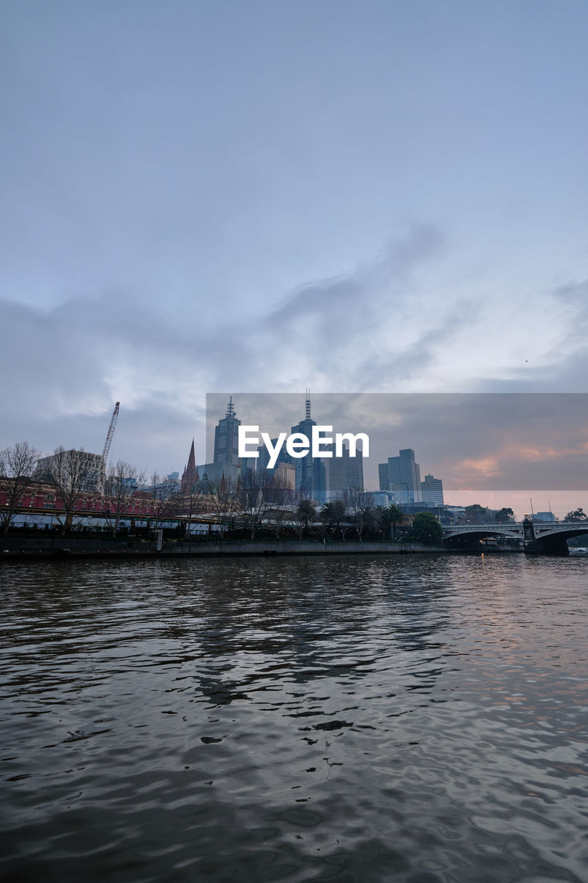 View of buildings by river against sky at dawn.