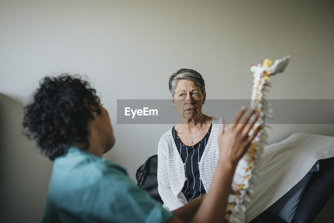 Multiracial doctor and patient discussing over spine model in clinic