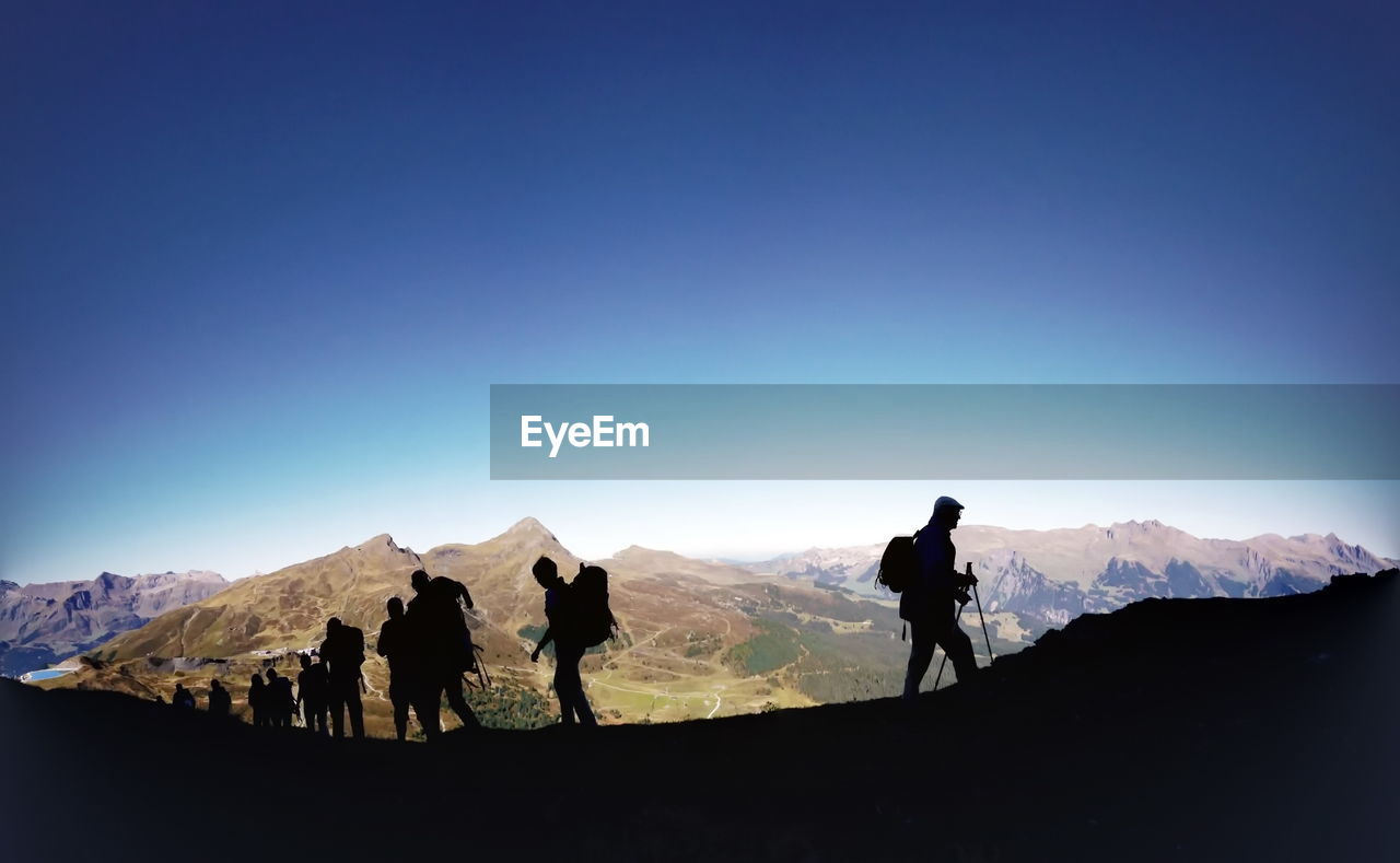 Silhouette hikers hiking on mountain against blue sky