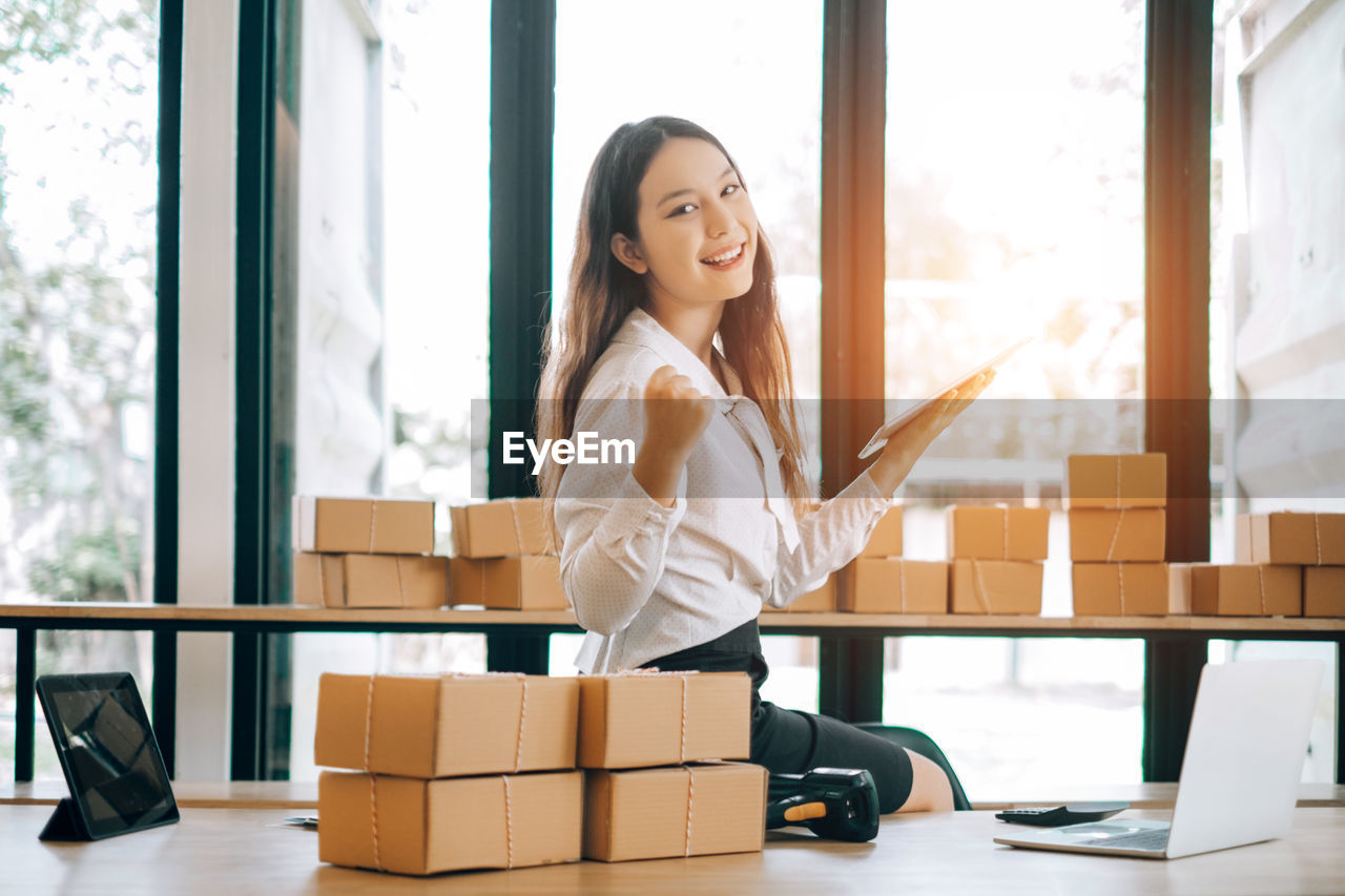 Portrait of young businesswoman working while sitting by packages at office