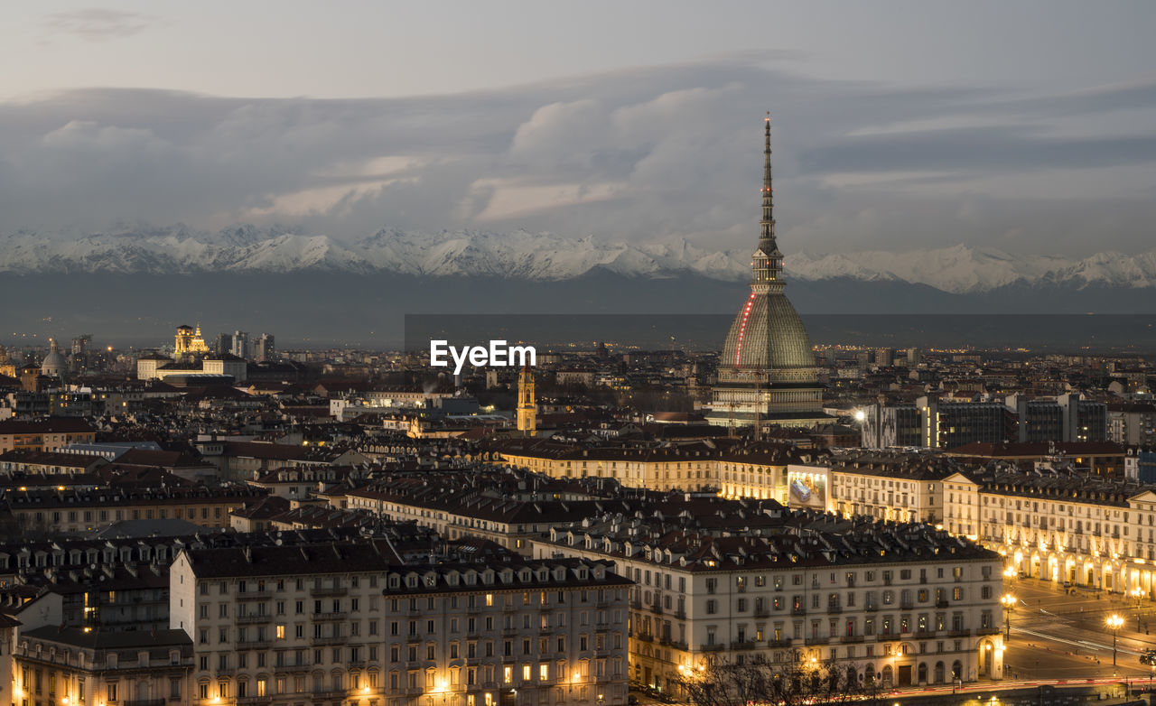 Illuminated buildings in city against cloudy sky