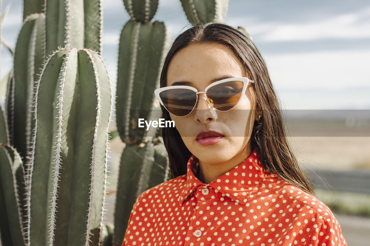 Confident young woman with sunglasses standing in front of cactus plant