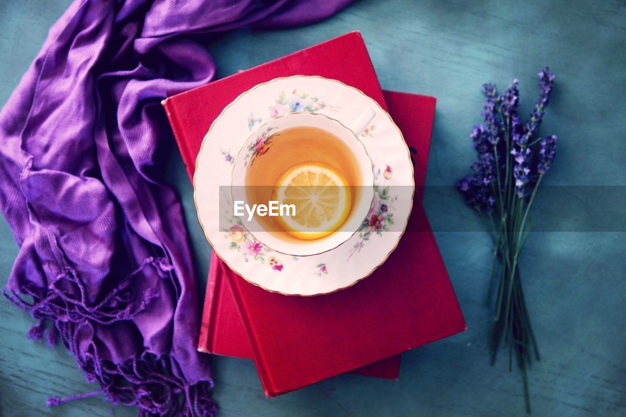 Directly above shot of tea on books by fabric and flowers on table