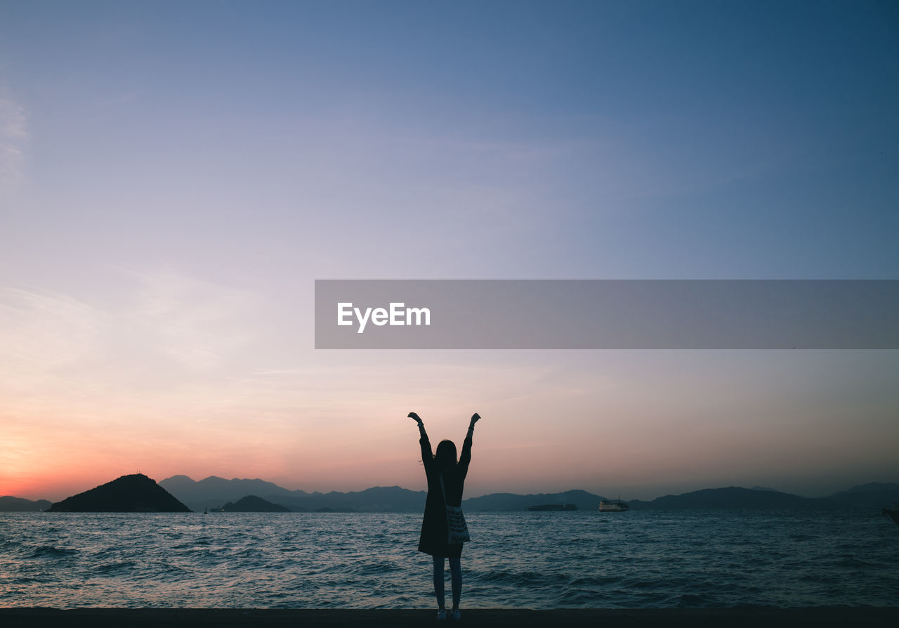 Woman with arms raised standing at sea shore against clear sky