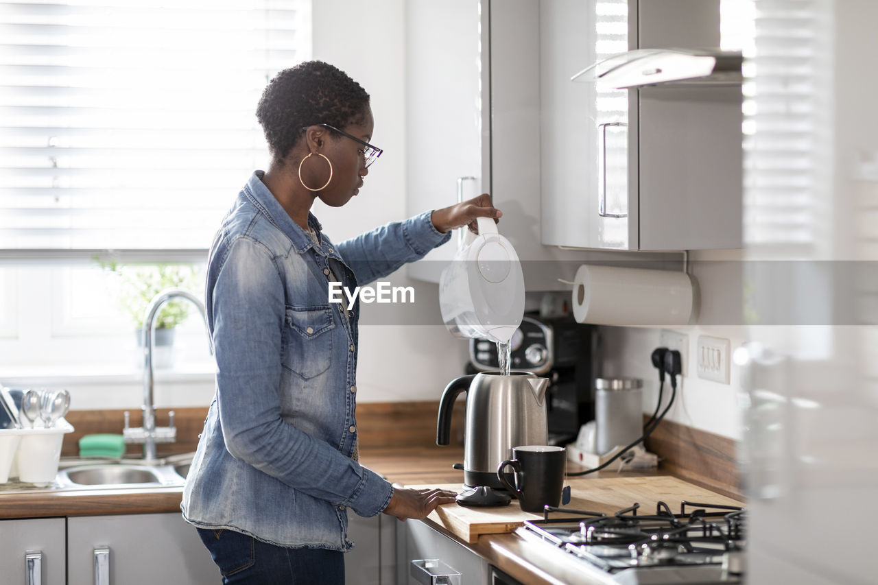 Woman pouring water into kettle in kitchen