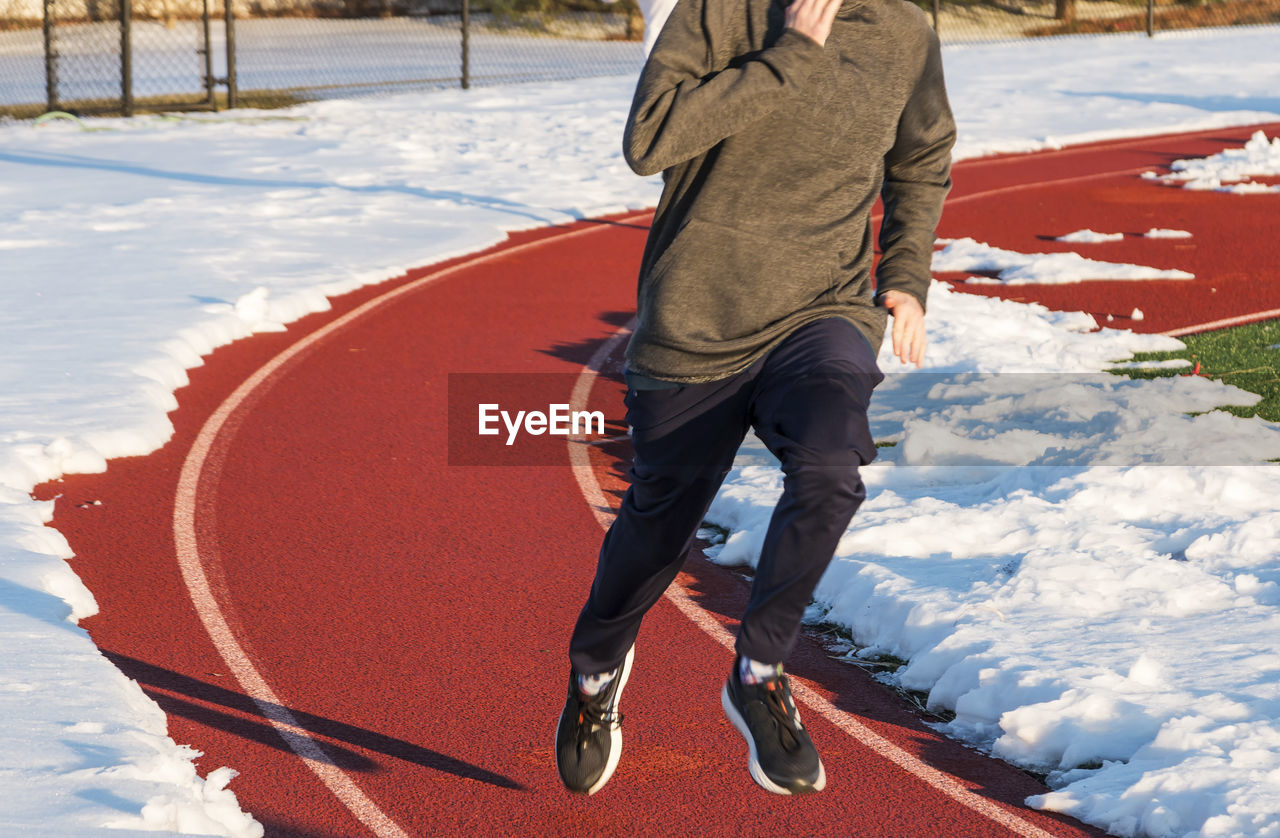 Low section of man running on sports track during winter