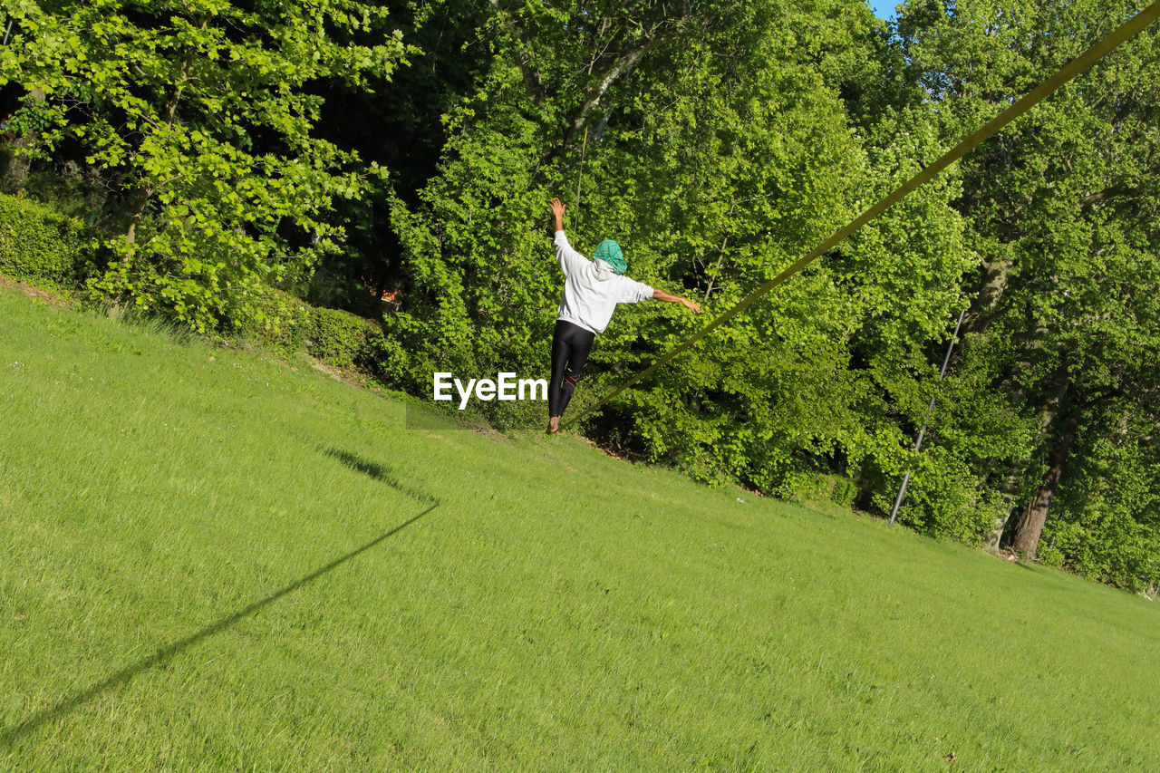 Rear view full length of man slacklining on grassy field during sunny day