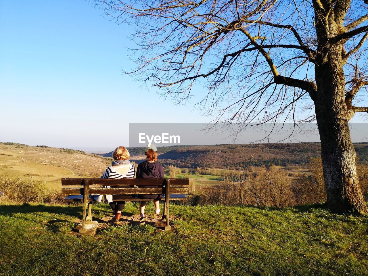 People sitting on bench against clear sky