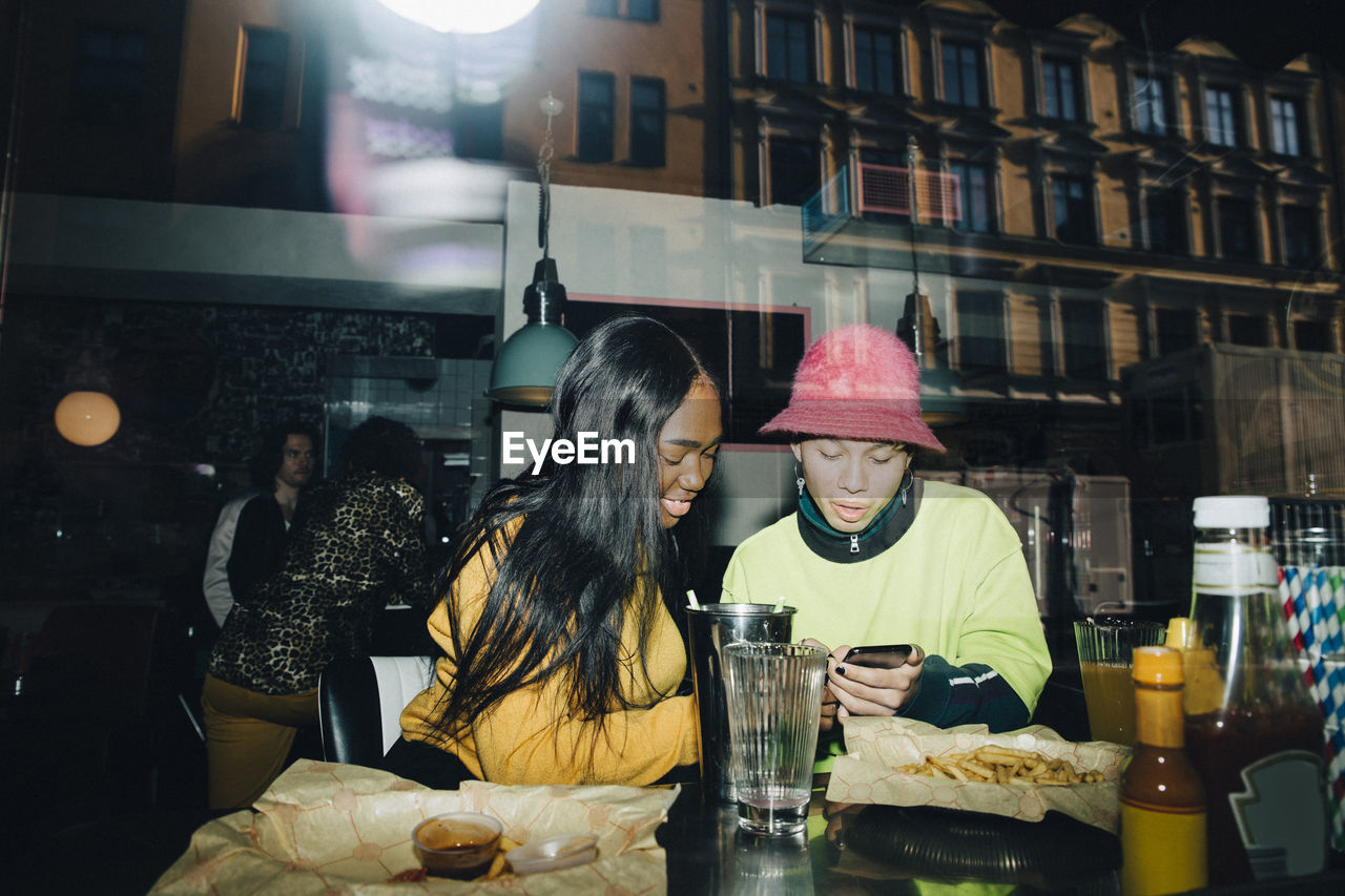 Man showing smart phone to smiling woman seen through transparent glass window