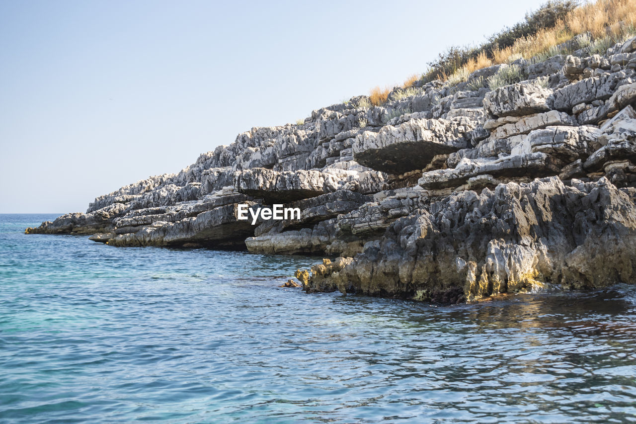 ROCK FORMATIONS IN SEA AGAINST CLEAR SKY