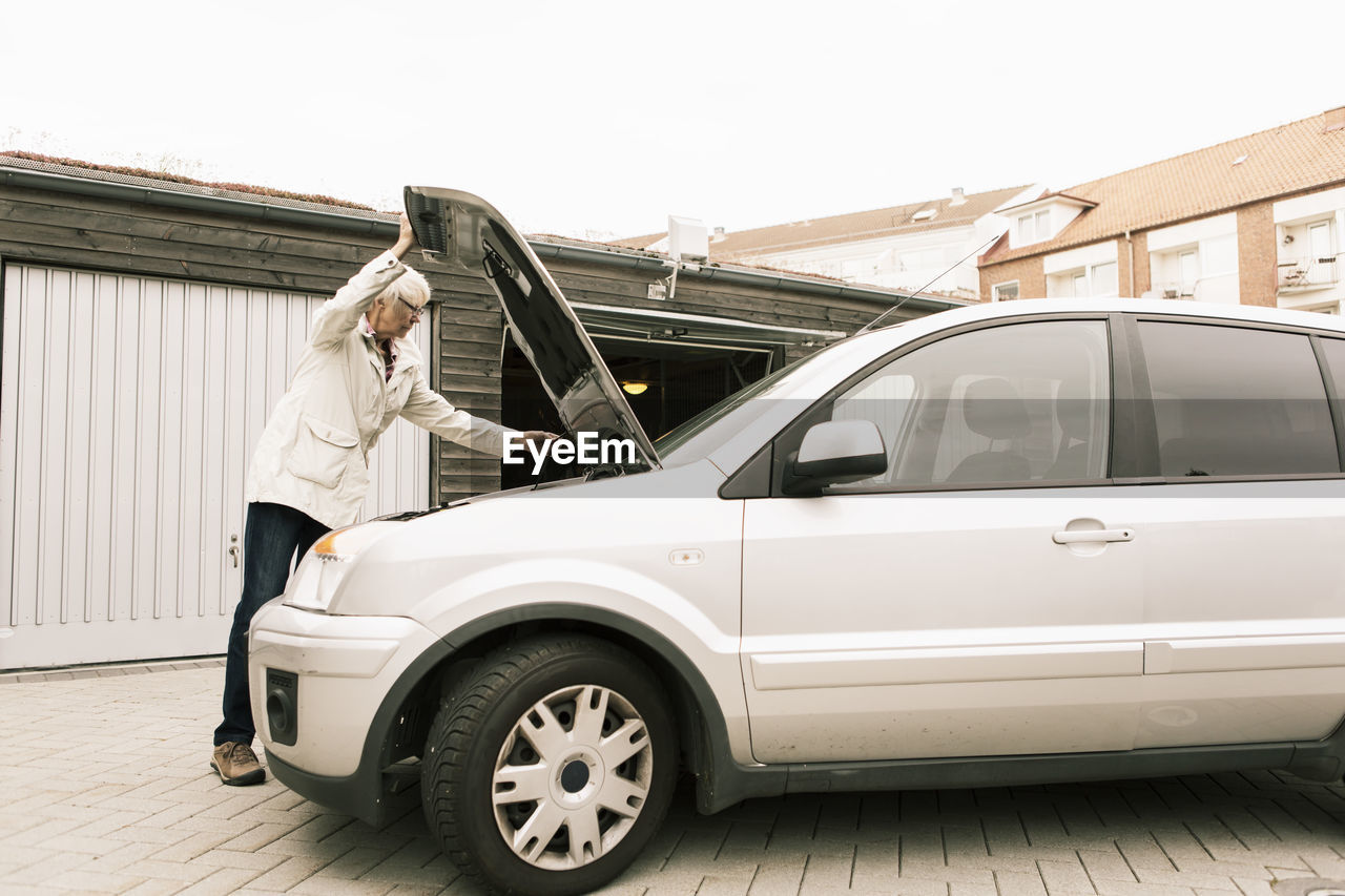 Senior woman opening car hood while standing by warehouse