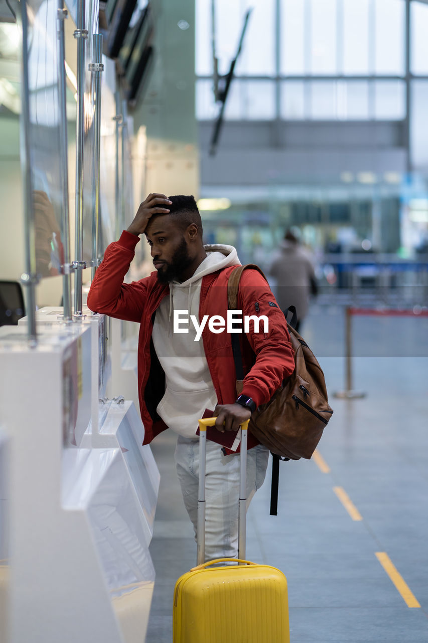 Upset african man standing at check-in counter in airport, being sad about moving away