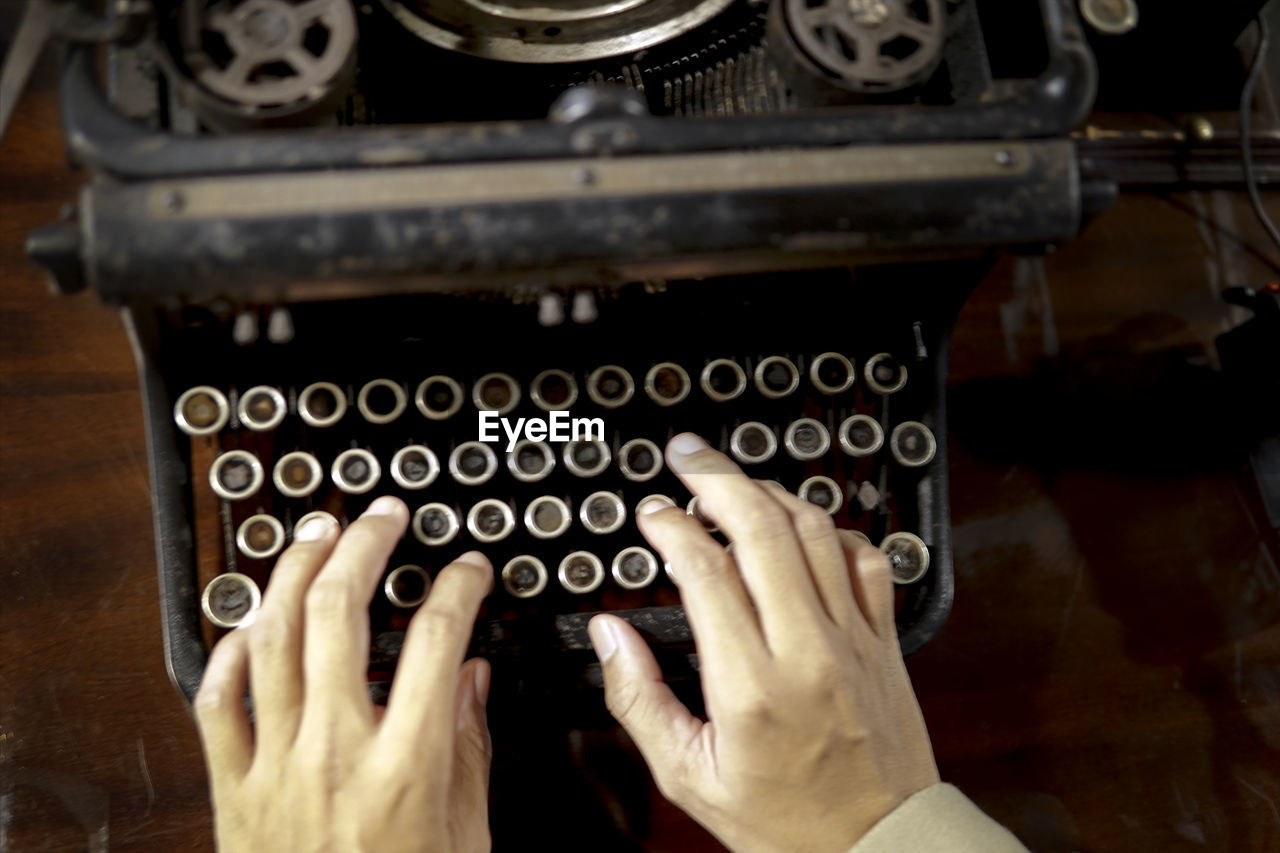 Cropped hands of person typing on vintage typewriter at table