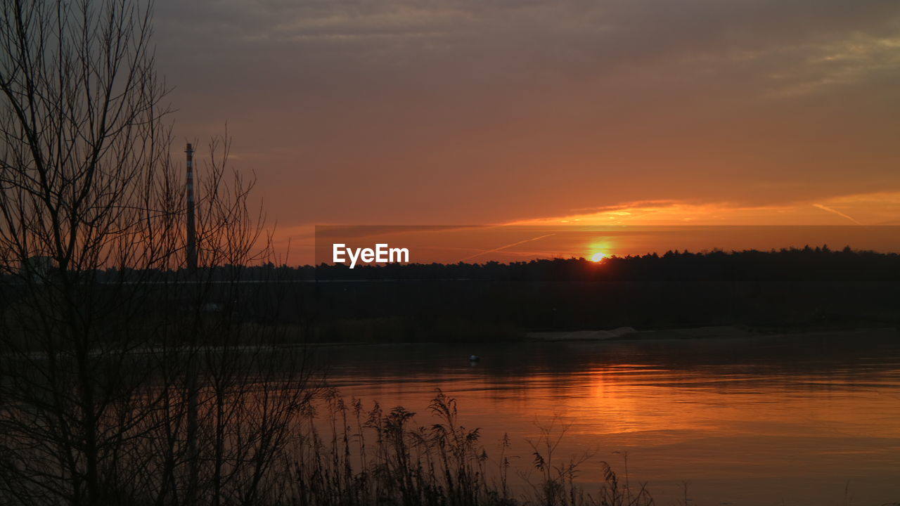 REFLECTION OF SILHOUETTE TREES IN LAKE AGAINST SKY DURING SUNSET