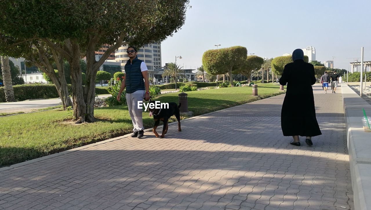 REAR VIEW OF PEOPLE WALKING ON PARK