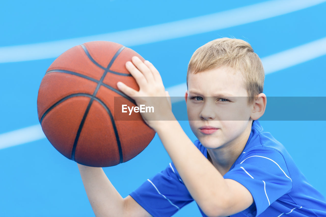 Portrait of boy holding basketball while standing on sports court