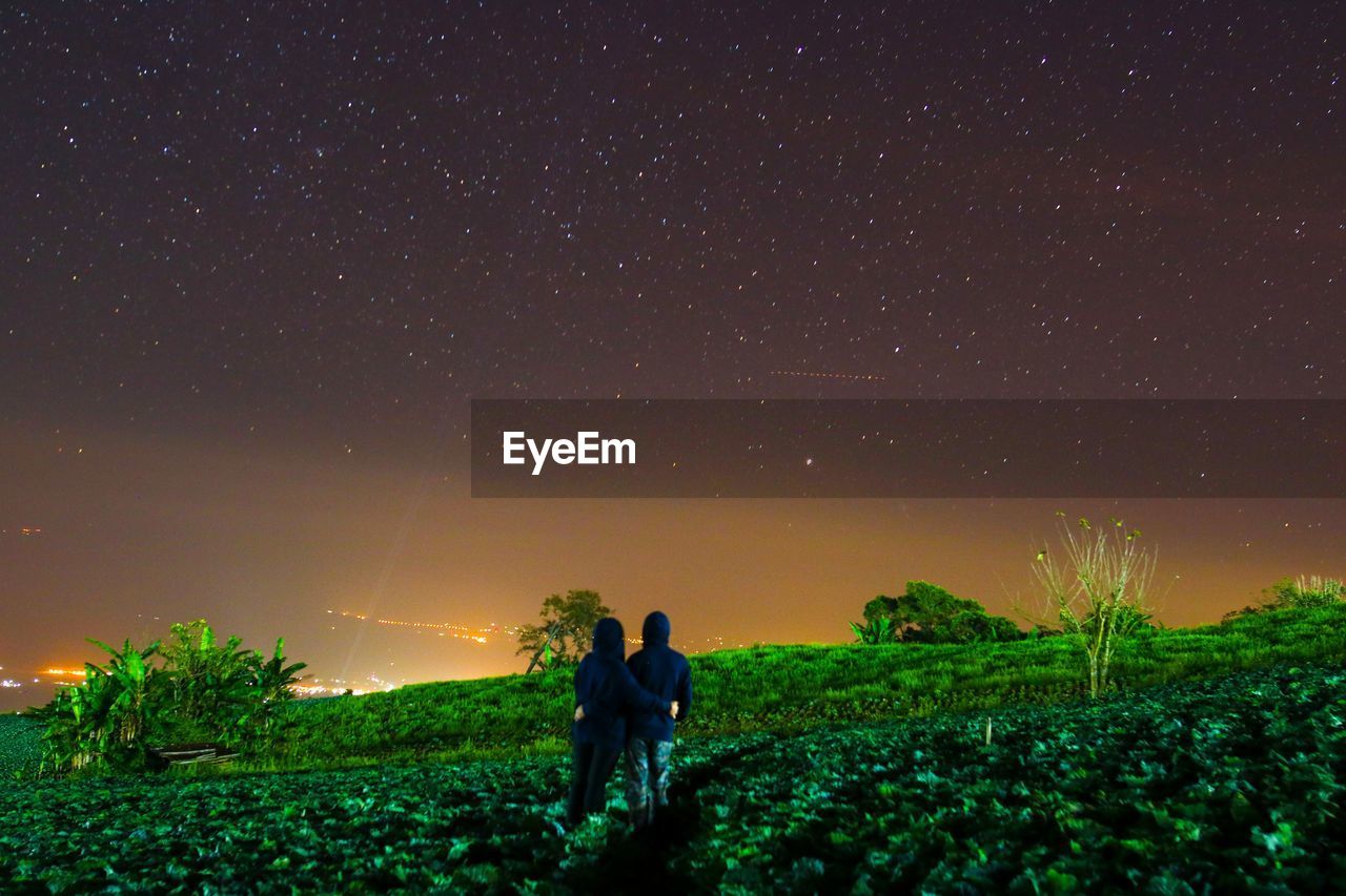 Rear view of men looking at star field against sky during night