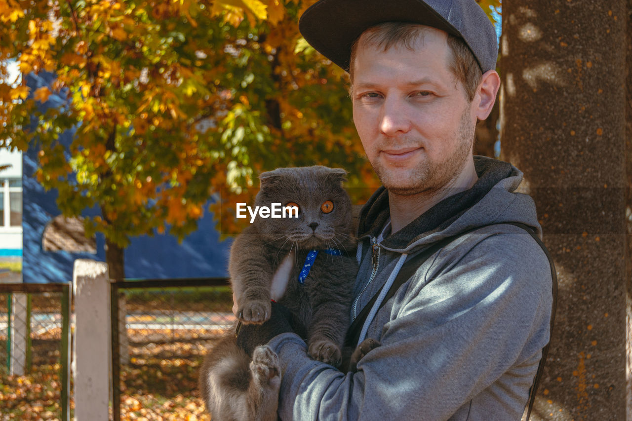 animal, animal themes, portrait, mammal, one person, looking at camera, adult, men, autumn, one animal, smiling, nature, animal wildlife, emotion, hat, clothing, holding, tree, domestic animals, happiness, day, waist up, outdoors, pet, positive emotion, plant, love, leisure activity, standing