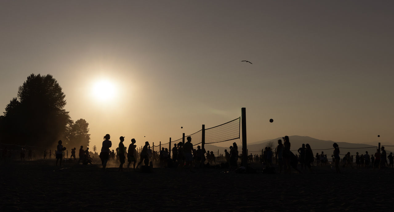 Silhouette people playing volleyball at beach during sunset