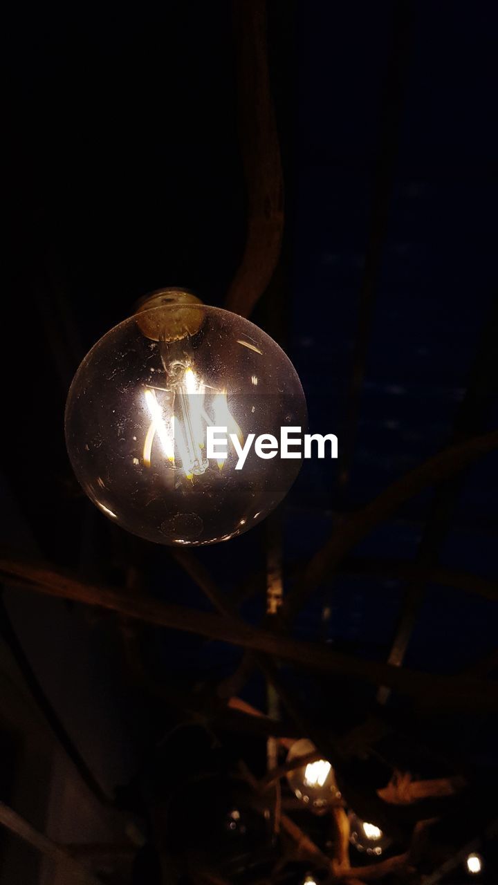 LOW ANGLE VIEW OF ILLUMINATED LIGHT BULB HANGING AT NIGHT