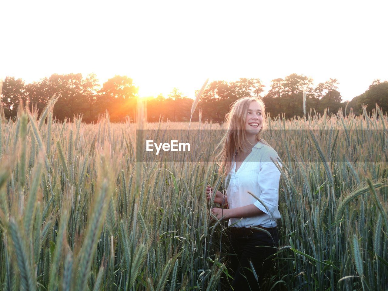 Happy woman standing amidst wheat field against sky during sunset