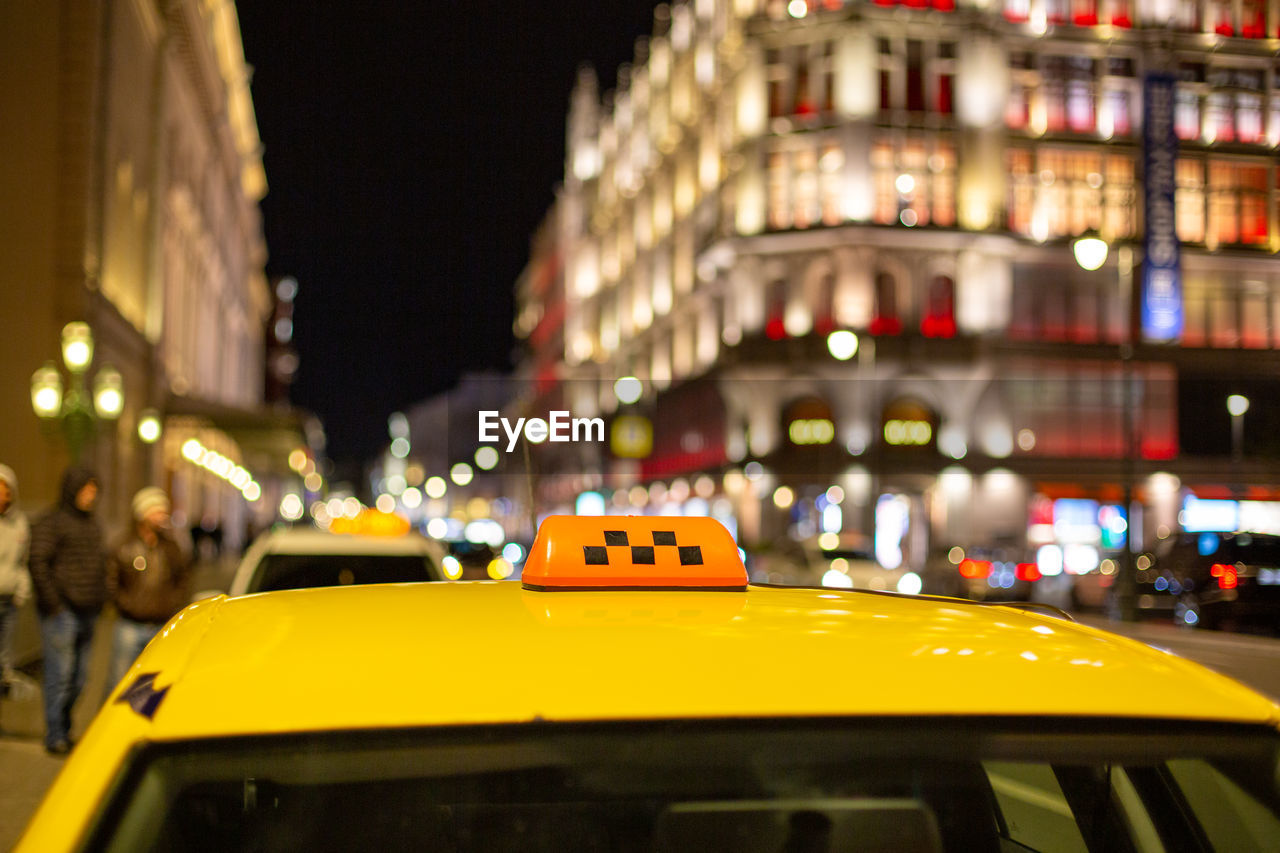 YELLOW CAR ON STREET AGAINST ILLUMINATED BUILDINGS IN CITY