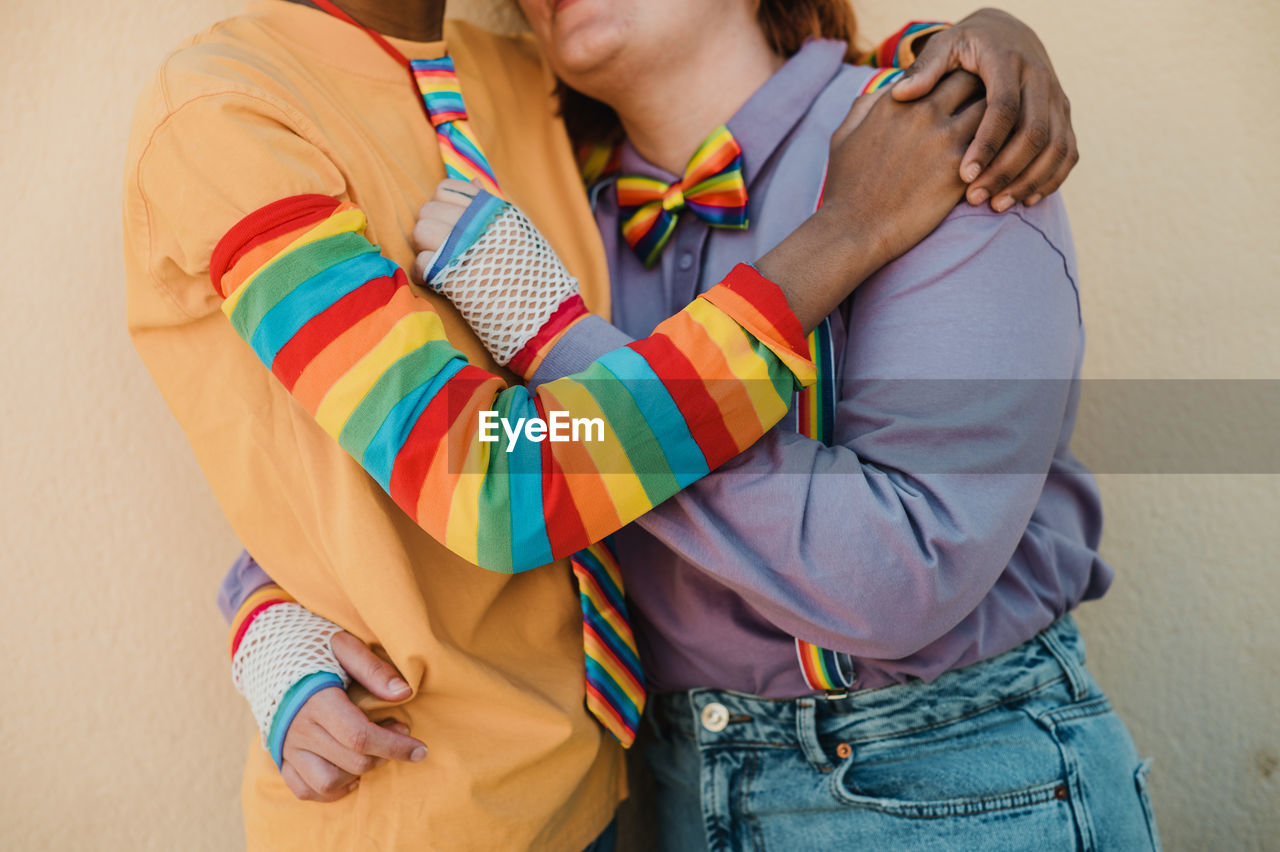 Loving multiethnic lesbian couple in rainbow accessories hugging tenderly