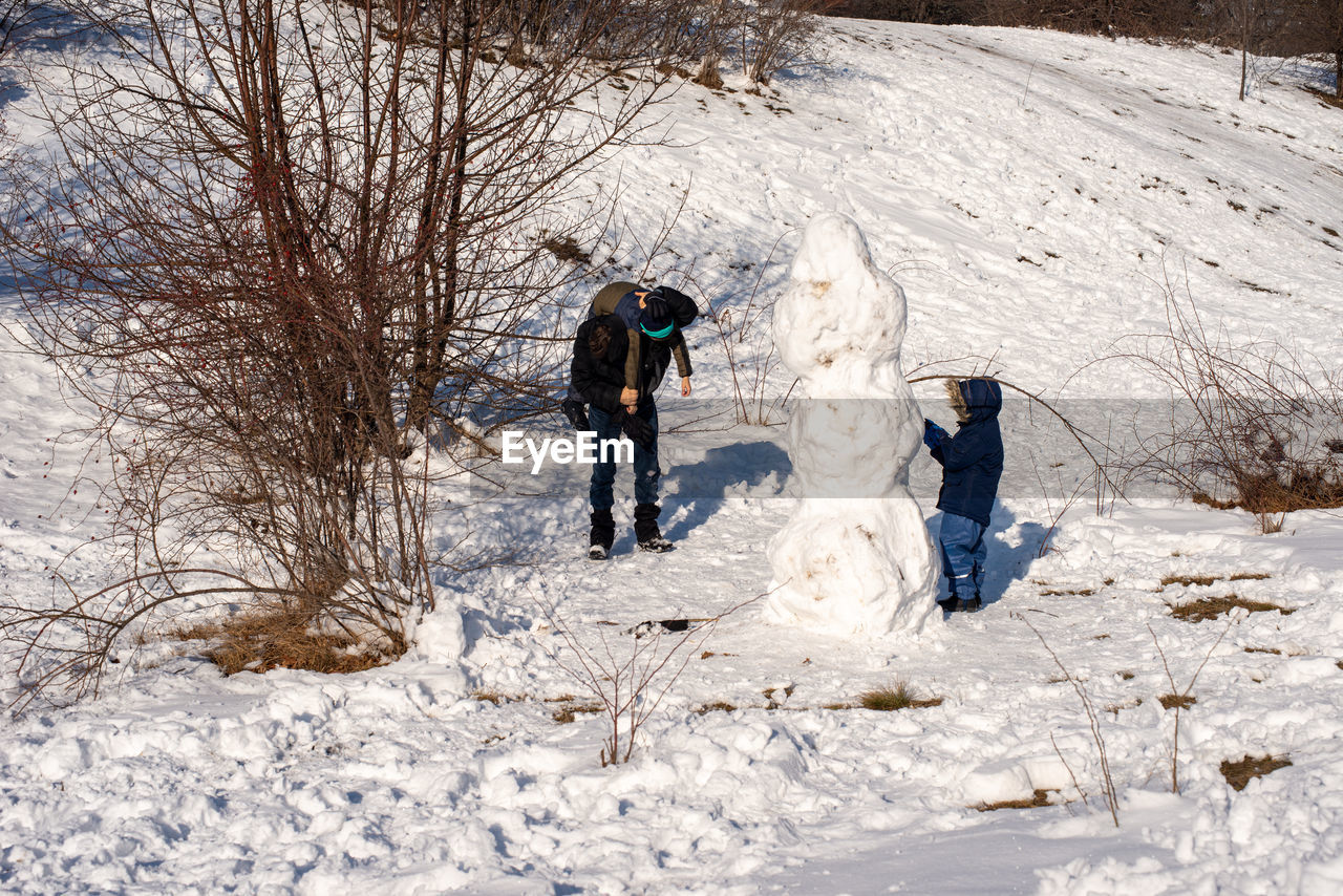 Father playing with children around snowman. fun in the park.