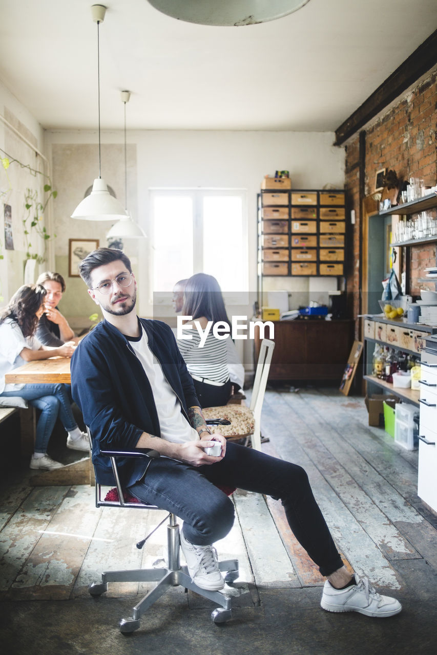 Portrait of confident young male it expert sitting on chair in creative office