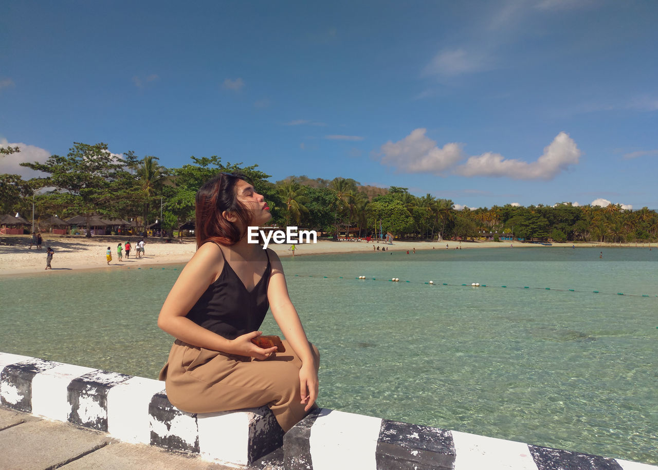 Young woman sitting on beach against sky