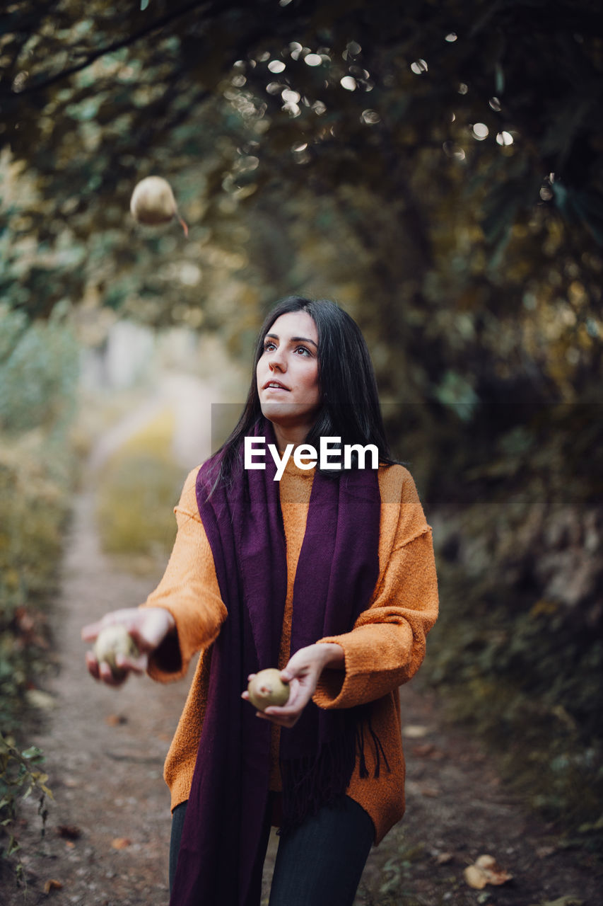 Woman wearing scarf juggling fruits in forest