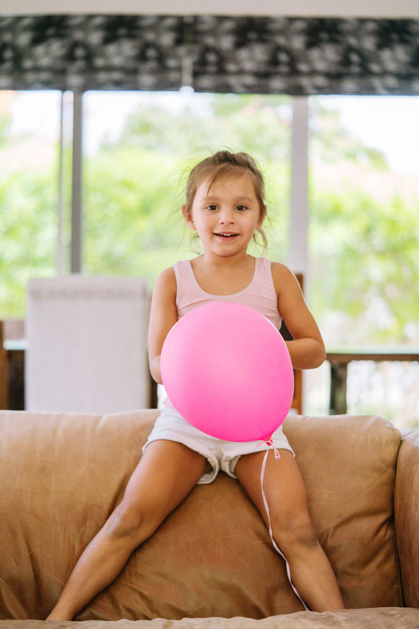Little girl playing with a pink balloon at home