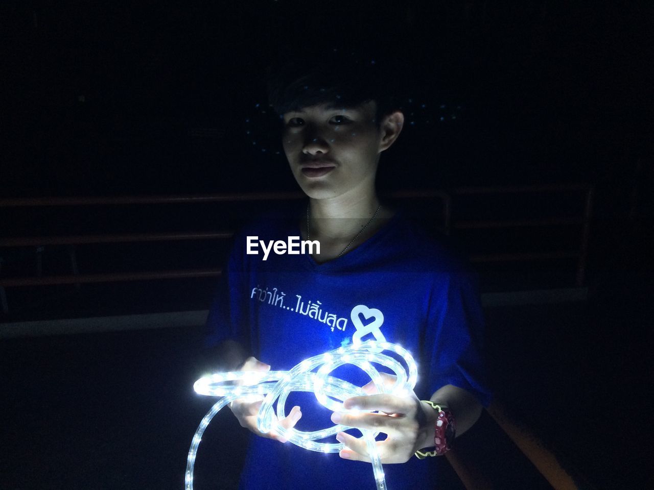 Young man holding illuminated lighting equipment while standing on balcony at night